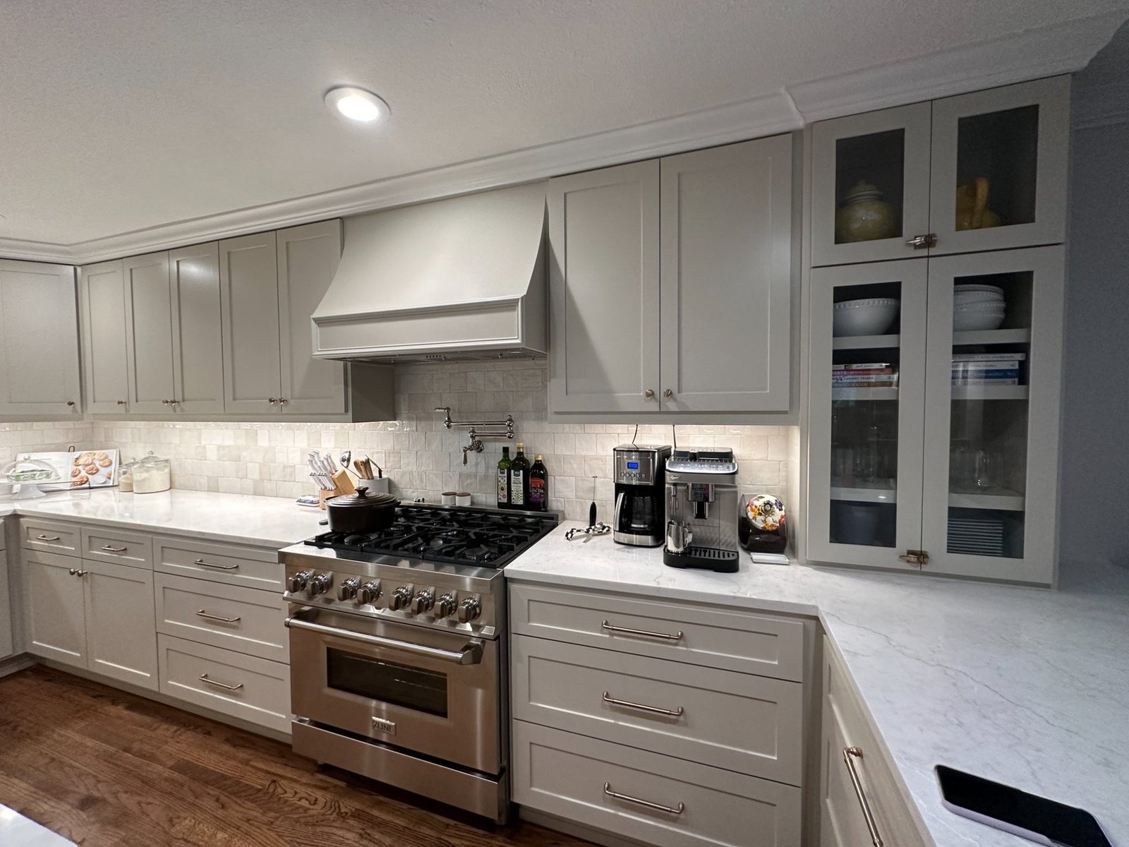 Warm gray kitchen with custom range hood and glass front cabinets